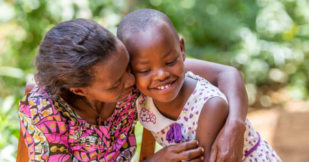 Umiwama, Uwase's mum, gives her a hug and a kiss on the cheek. Both of them are smiling warmly.