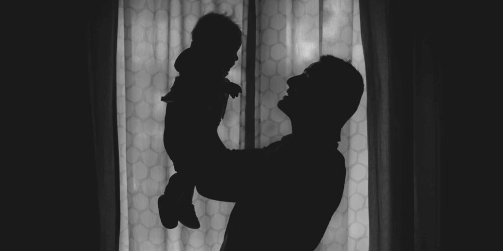 A silhouette of a father holding up his child, offering a contrast to the harrowing conditions described by Barry Bogin in his research.
