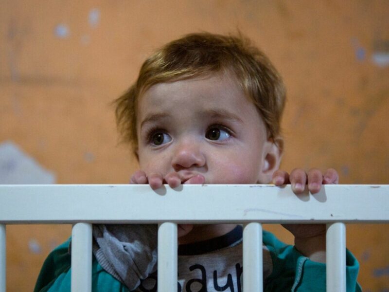 A child at risk of ending up in an orphanage, peeking their face over the edge of a cot
