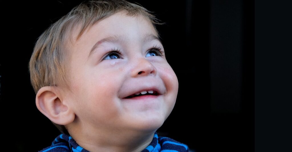 Esmerelda's son Haris looks up and smiles with a tear in his eye.