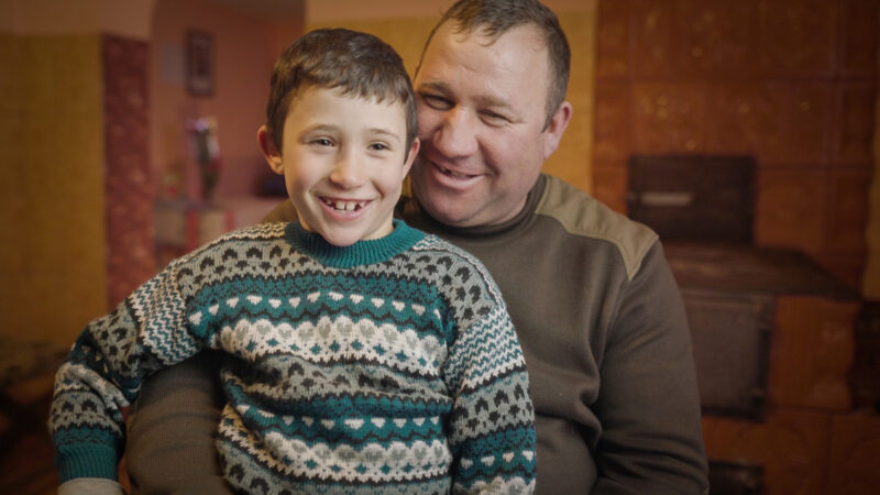 Nelu* sitting on his uncle, Ion's* knee in their kitchen,