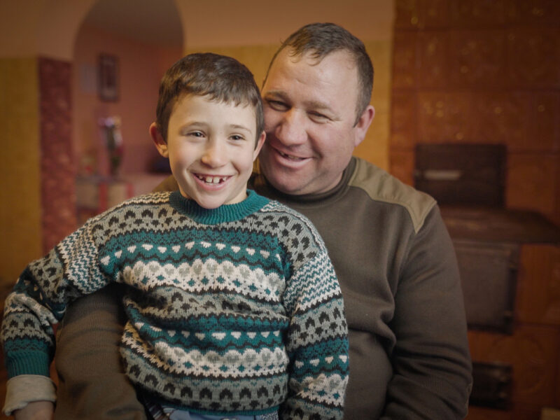 Nelu* sitting on his uncle, Ion's* knee in their kitchen,