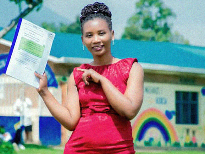 A young woman in a red dress points at her graduation certificate