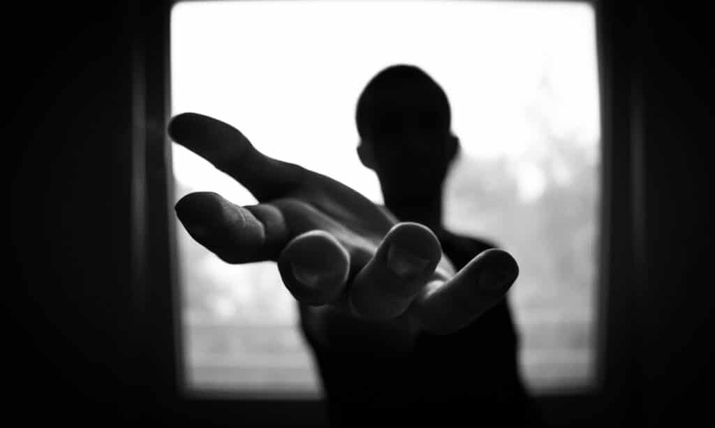 A young person in silhouette reaches out their hand towards the camera.