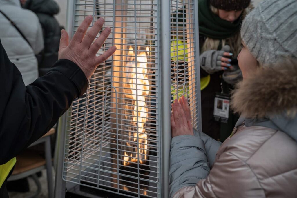 People warming their hands over a mobile flame-fuelled heater.