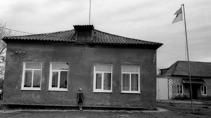 Black and white picture of a soviet style orphanage exterior with a child standing out front
